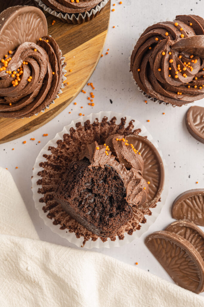 Chocolate Orange Cupcake with a bite missing laying on a cupcake wrapper on a table.