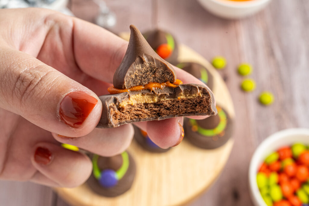 A Peanut Butter Witch Hat Cookie with a bite taken out of it being held by a hand.