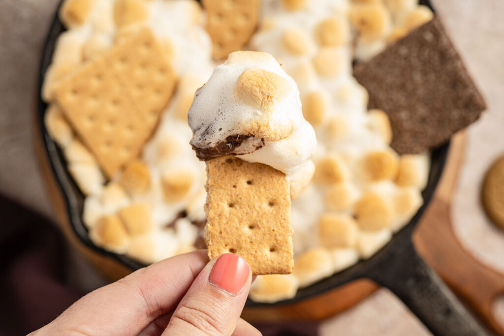 S'Mores Dip on a graham cracker above a skillet filled with S'Mores Dip.