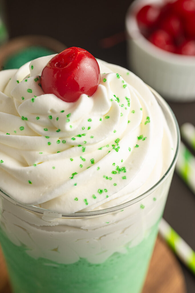 A close up of whipped cream and a cherry on top of a Shamrock Shake.
