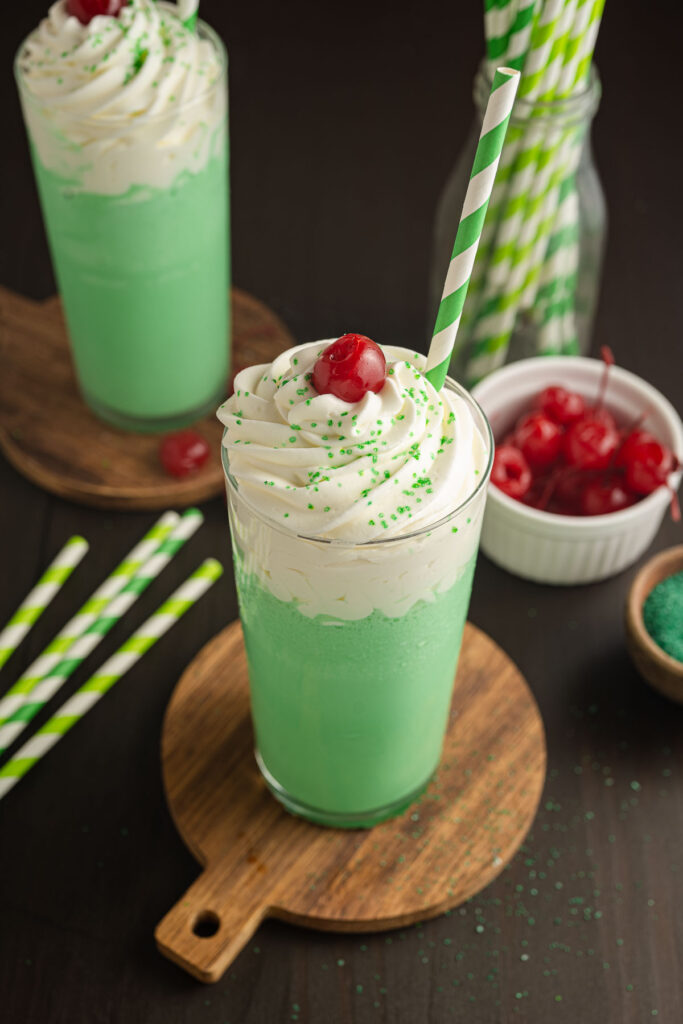 Two shamrock shakes on coasters on a wooden table.