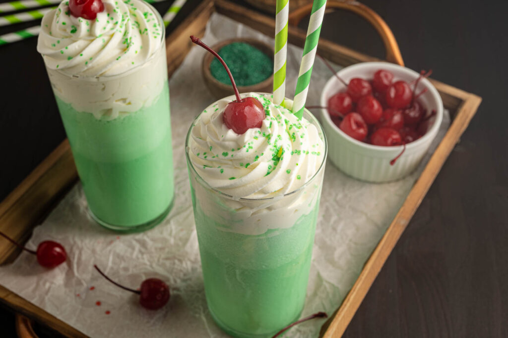 A couple of homemade Shamrock Shakes on a wood tray with cherries.