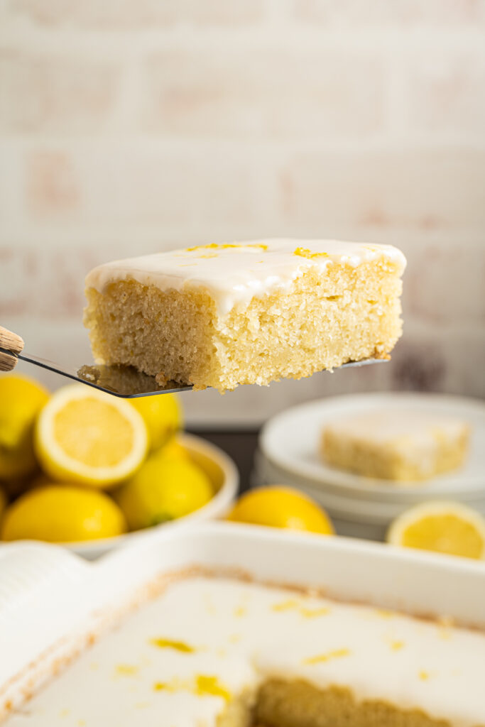 A slice of eggless lemon cake being held on a cake server.