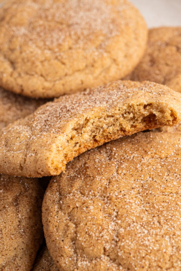 Maple Snickerdoodles piled on a plate with one with a bite taken out of it.