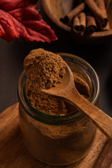 Homemade pumpkin pie spice in a small jar with a small spoonful on top.