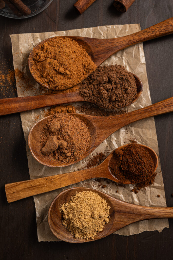 Spoons full of spices that make up Homemade Pumpkin Pie Spice laid out on parchment paper.