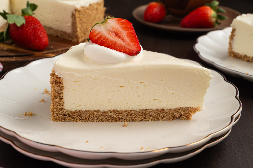 A slice of no bake cheesecake on a plate with a strawberry and whipped cream on top.