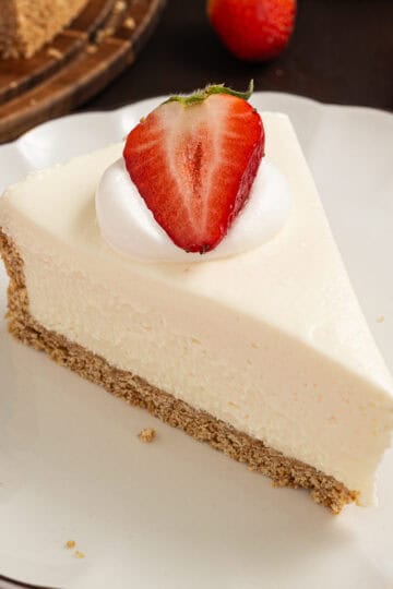 A slice of no bake cheesecake with half a strawberry on top on a white plate.